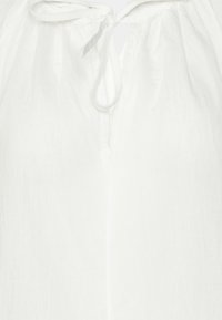 Haut en tissu léger blanc avec une petite ouverture en V et un détail de noeud attaché au niveau du col.