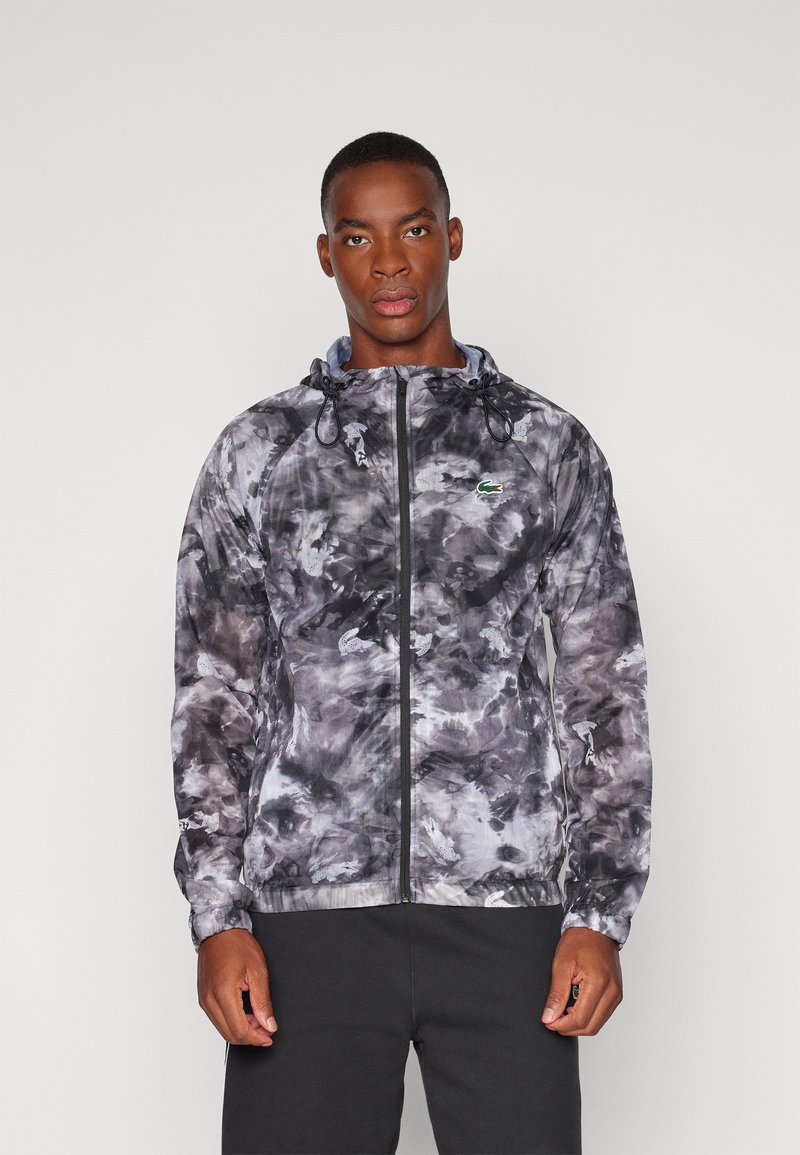 Chaqueta ligera con cremallera en un patrón de teñido anudado en negro y gris, con capucha, cordón y logo bordado en el pecho.