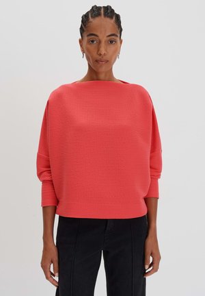 Coral textured long-sleeve sweater with a wide neckline and cuffed sleeves, paired with black straight-leg pants.
