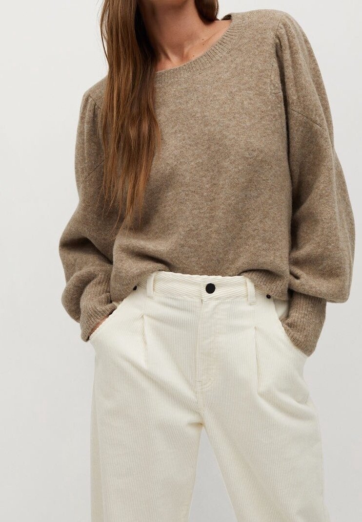 Femme portant un pull beige ample à manches ballon, rentré dans un pantalon en velours côtelé écru taille haute, les mains dans les poches.