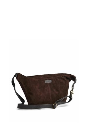 Sac bandoulière en suède marron avec une sangle en cuir noir réglable et une boucle métallique, présenté sur fond blanc.