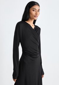 Black long-sleeve dress with a wrap design, soft fabric, and draped texture, featuring a V-neck and fitted silhouette.