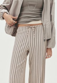 Světle šedá bomber bunda s květinovou výšivkou, ribbed šedý top a pruhované široké kalhoty v béžové a tmavě šedé barvě s elastickým pasem.