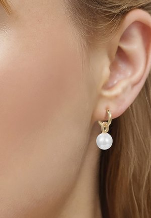 Guld ørering med små sammenkoblede ringe og en enkelt hvid perle, der hænger fra en kvindes øre med lys hud og blondt hår.