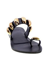 Sandalo piatto nero con una larga fascia che presenta dettagli metallici dorati simili a borchie arrotondate. Design aperto sulla punta e sul retro con un anello per l'alluce.