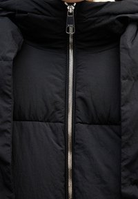 Gros plan d'une veste matelassée noire avec une fermeture éclair argentée brillante partiellement fermée.