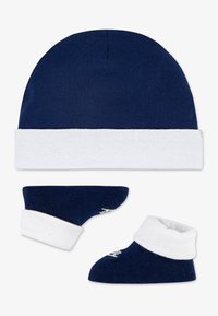 Ναυτικό καπέλο από βαμβάκι με λευκό μπατζάκι και αντίστοιχα μποτάκια. Τα μποτάκια διαθέτουν αναδιπλούμενο μπατζάκι και διακριτικό σχέδιο, και είναι και τα δύο μαλακά και άνετα.