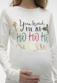 Hvid langærmet skjorte med et festligt grafisk design. Teksten i sort, rød, grøn og guld siger "Du fik mig ved HO HO HO" med kristtorn-dekorationer.