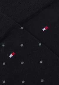 Schwarze Socken aus weichem Stoff mit kleinen grauen Punkten und einem rot-weißen und blauen Logo. Glatte Textur mit einem dezenten Muster.