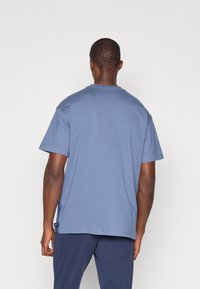 Kortærmet blå bomulds T-shirt med rund hals, afslappet pasform og sidelabel detalje nær kanten. Glat tekstur og ensartet farve.