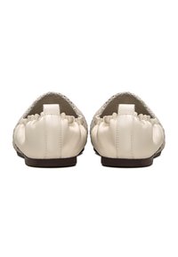 Zapatos de cuero sin cordones con una textura trenzada. Color crema, con un suave respaldo redondeado, sutiles volantes y suela plana. Diseñados para la comodidad.