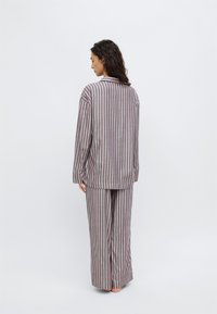 Conjunto de pijama a rayas que incluye una camiseta de manga larga y pantalones de pierna ancha en gris con rayas rosas y moradas. Tejido suave, ajuste relajado, sin cierres.