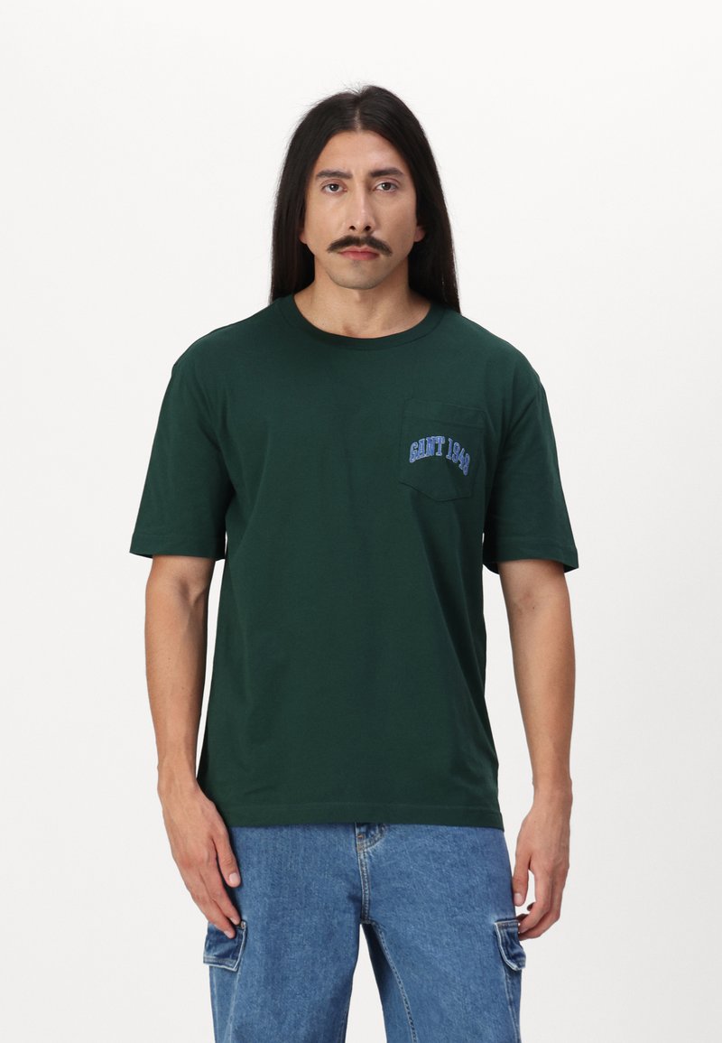 Mørkegrøn bomulds t-shirt med korte ærmer og rund halsudskæring. Har en lille blå broderet lomme med "GANT 1949." Standard pasform.