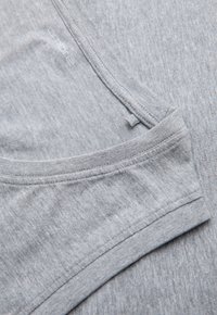 Tissu de t-shirt en coton gris clair doux montrant un gros plan du col et des bords des manches avec des coutures visibles et une étiquette de taille M 48 à l'intérieur.