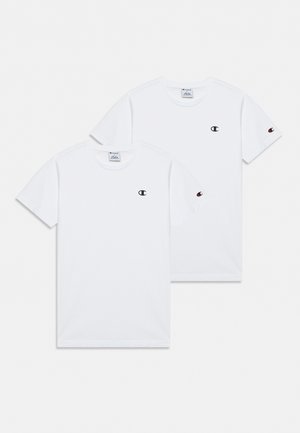 Deux T-shirts Champion blancs à manches courtes se chevauchent sur un fond clair. Chacun porte un petit logo sur la poitrine et sur la manche.