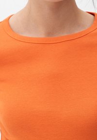 T-shirt in cotone arancione con scollatura tonda, texture liscia e maniche corte, che presenta una silhouette aderente.