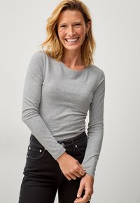 Grijze lange mouwen shirt gemaakt van zachte stof, met een ronde halslijn, gecombineerd met zwarte jeans en minimalistische zilveren hardware details.
