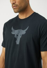 Black t-shirt made of soft material featuring a large gray bull head logo on the front. Short sleeves and a crew neckline.