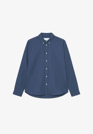 Chemise boutonnée bleu marine avec une texture douce, col structuré et boutons blancs. Présente un petit logo sur la poitrine gauche.