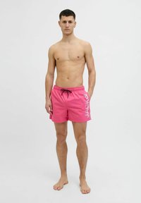 Roze zwembroek met een elastische tailleband en trekkoord. Voorzien van een groot wit logo aan de zijkant. Gladde textuur en lengte boven de knie.