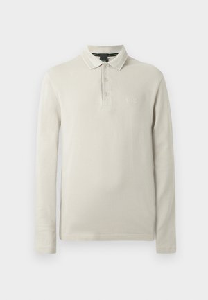 Polo majica dugih rukava u svijetlo bež boji, izrađena od mekanog materijala. Ima ovratnik, plisu s tri gumba i diskretni vezani logo na prsima.