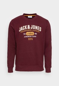 Bordeauxfarbenes Sweatshirt mit Rundhalsausschnitt, das mit weißem und gelbem Text sowie gerippten Bündchen und Saum versehen ist. Der Stoff hat eine weiche Textur.