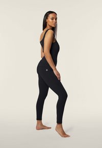 Bodysuit de activewear negro con una tirante y espalda descubierta, combinado con leggins negros de cintura alta, ambos en una tela suave.