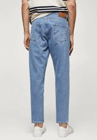 Jeans in denim azzurro chiaro con taglio dritto, due tasche posteriori e un patch in pelle marrone sulla cintura, abbinati a scarpe bianche.
