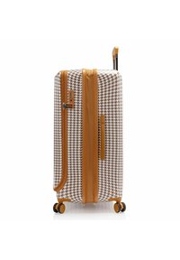Maleta rígida con un patrón de houndstooth marrón y blanco, acentos beige, un asa lateral y cuatro ruedas negras para mayor movilidad.