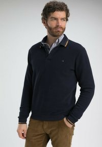 Sweatshirt polo à manches longues bleu marine avec des poignets côtelés et un col contrastant, associé à un pantalon en velours côtelé marron.
