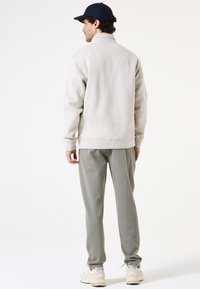 Sudadera gris claro con un cuello alto, combinada con pantalones texturizados verde claro y una gorra de béisbol azul marino. Ajuste casual y relajado.