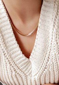 Collar de cadena de oro con un diseño liso y elegante, reposando sobre un tono de piel, combinado con un suéter de punto blanco texturizado.