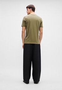 Olivovo zelené tričko s krátkym rukávom a okrúhlym výstrihom, v kombinácii s čiernymi širokými nohavicami, z pohľadu zozadu, na neutrálnom pozadí.