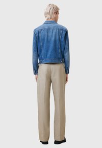 Jeansjack in een vervaagde blauwe kleur en klassiek ontwerp, met een knoopsluiting, twee achterzakken en lange mouwen. Gepaard met beige broek.