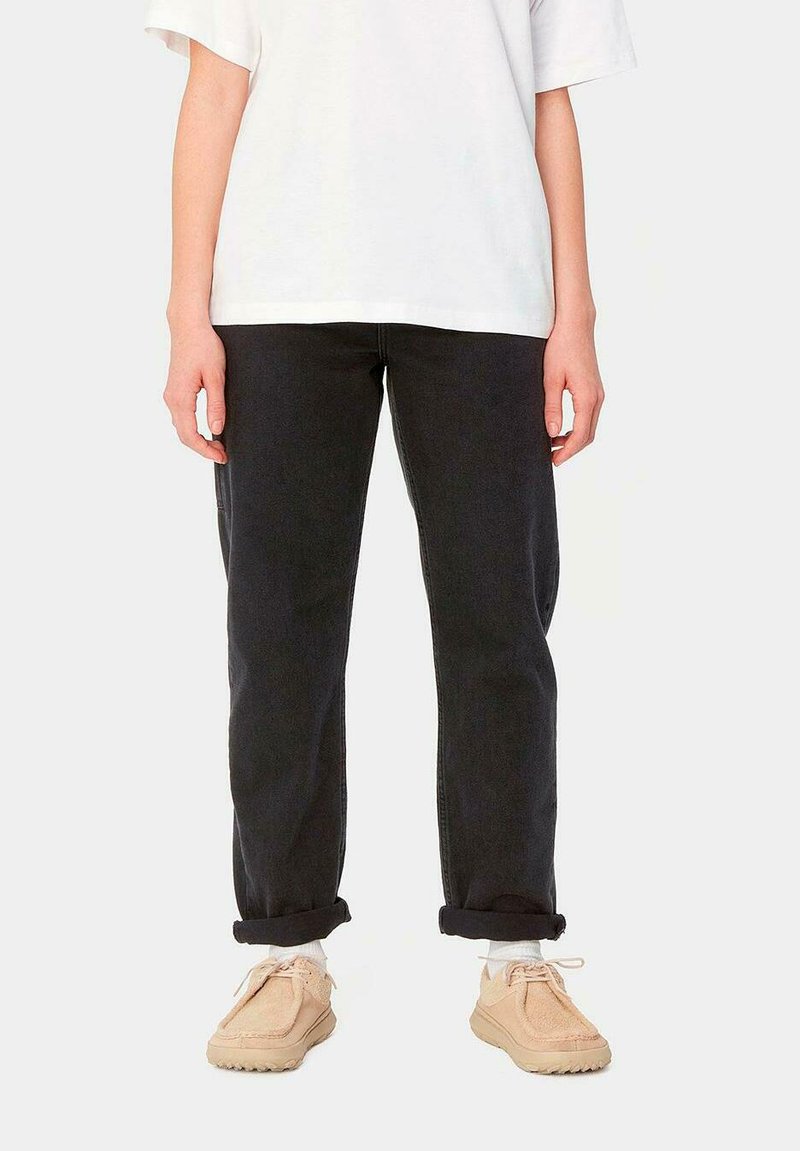 Vaqueros de mezclilla negros con un corte relajado y puños enrollados, combinados con zapatillas beige. La parte superior es una camiseta blanca de corte holgado.