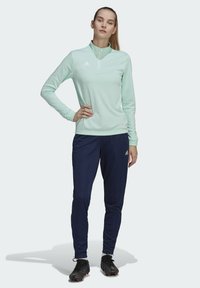 Helles Mint langärmliges Sportoberteil mit Viertelreißverschluss, kombiniert mit marineblauen Hosen. Beide tragen das Adidas-Logo, haben ein strukturiertes Gewebe und eine körpernahe Passform.