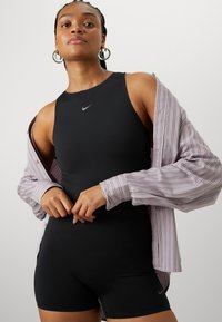 Crni Nike bodysuit s okruglim izrezom, uparen s razdovrenom prugastom majicom ljubičaste i bijele boje. Bodysuit ima akcent loga.