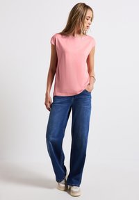 Haut rose à manches courtes avec une coupe décontractée, assorti à un jean large bleu, tous deux en tissu doux. Des chaussures décontractées complètent l'ensemble.