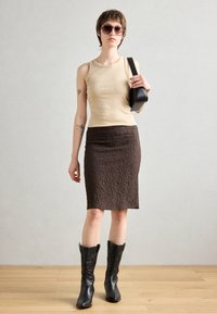 Beige singlet, teksturert brun blyantskjørt og svarte kne-høye støvler. Solbriller og en liten svart veske fullfører antrekket.