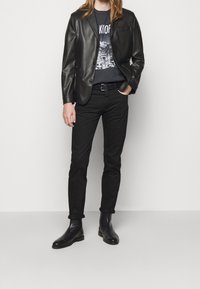 Svart läderblazer över en grafisk svart t-shirt, kombinerad med slim-fit svarta byxor och svarta ankelstövlar. Minimalistisk design, slät textur.