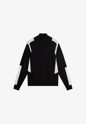 Zwart pullovertrui met een hoge kraag en een halve rits. Heeft witte geometrische panelen op de mouwen en de borst. Zacht gebreid materiaal.
