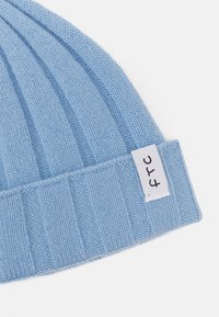 Light blue knit beanie with ribbed texture and a folded cuff. Features a small white tag with black lettering on the side.