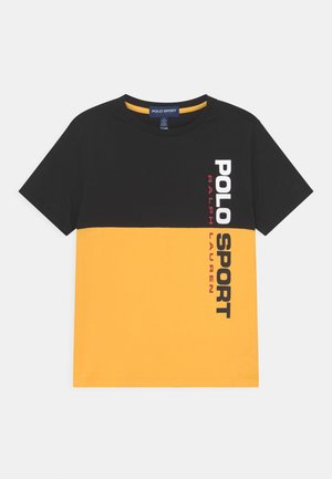 T-shirt à manches courtes avec moitié supérieure noire et moitié inférieure jaune, avec un texte vertical « POLO SPORT RALPH LAUREN » sur le côté droit.