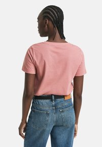 Roze t-shirt met korte mouwen en een ronde hals, gedragen met hoge blauwe spijkerbroeken met een zwarte riem en een gestructureerde stof.