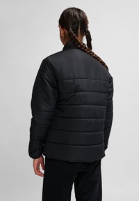 Sort isoleret jakke med quiltet design, lange ærmer og lige kant. Stoffet fremstår glat med en mat finish.