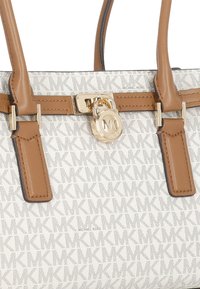 Borsa bianca a motivo con manici e rifiniture in pelle marrone, caratterizzata da un charm a lucchetto dorato MK e il marchio Michael Kors.