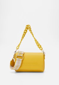 Gul läderhandväska med en flätad kedjesnodd och en randig tygaxelrem. Har präglad logotyp på framsidan.
