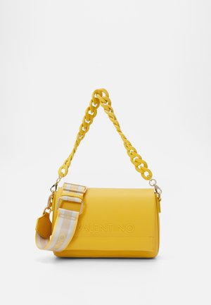 Žlutá kožená kabelka s pleteným řetízkem na rameno a pruhovaným látkovým popruhem. Na přední straně má vpředu ražené logo.