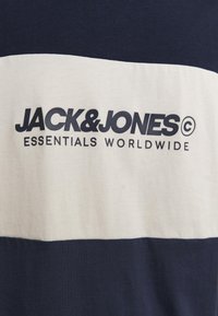 Marineblå og hvid stribet t-shirt med "JACK & JONES ESSENTIALS WORLDWIDE" trykt i mørkeblå på forsiden.