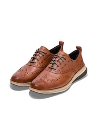 Scarpe in pelle marrone con dettagli brogue, dotate di una suola beige e lacci scuri. Il design include perforazioni e una forma snella.